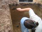 The archaeologist is carefully cleaning the profile wall of this test unit so she can map, photograph, and document the different layers of soil.